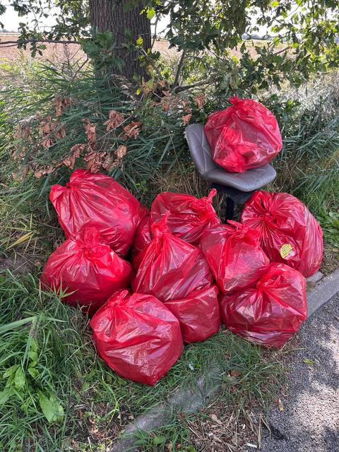 A pile of red rubbish sacks and a grey swivel chair under a tree at the roadside